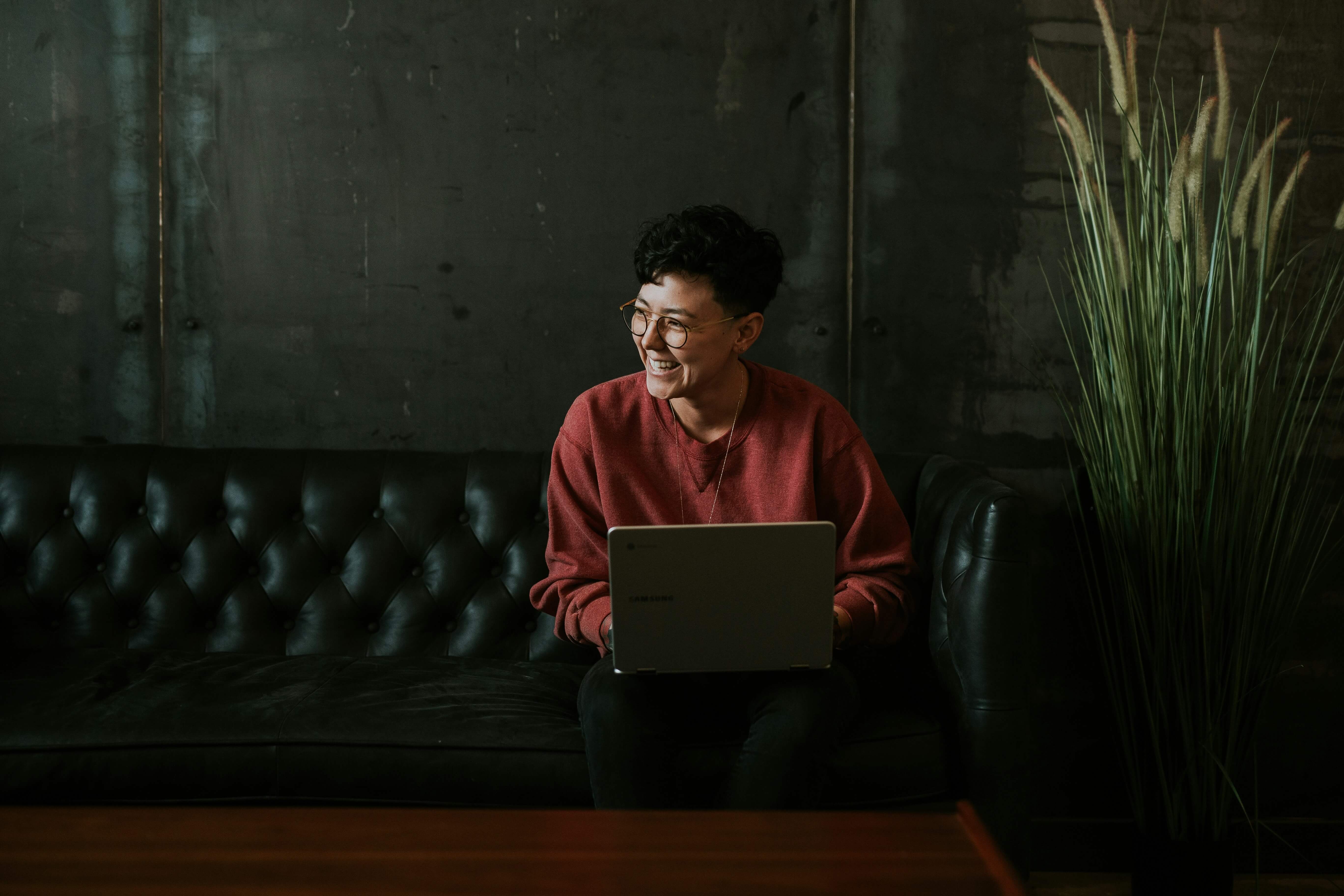 Woman with laptop smiling while sitting on an amazing, luxurious leather couch